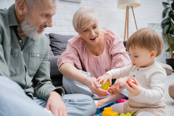 Positive middle aged couple playing building blocks game with little granddaughter in living room — Stock Photo