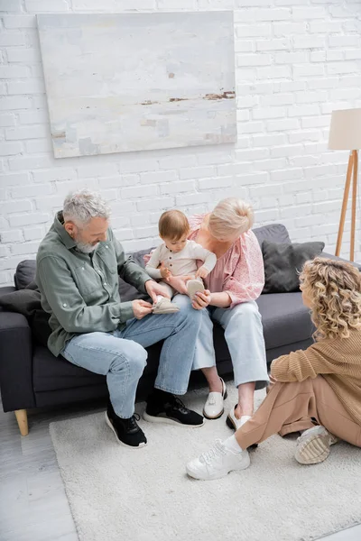 High angle view of middle aged couple sitting with little granddaughter on couch in living room — Stock Photo