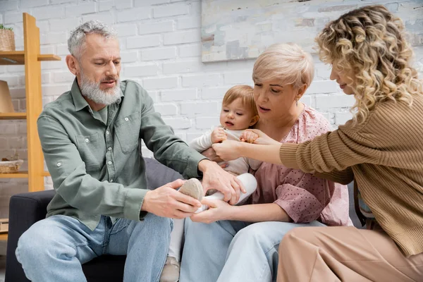 Woman holding hand of little daughter near mature parents on sofa at home — Stock Photo
