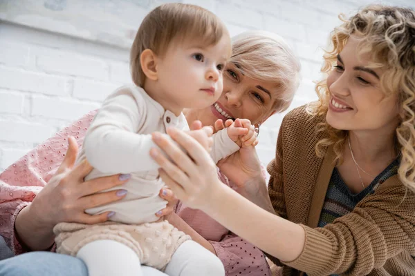 Little girl looking away near pleased mother and granny in living room — Stock Photo