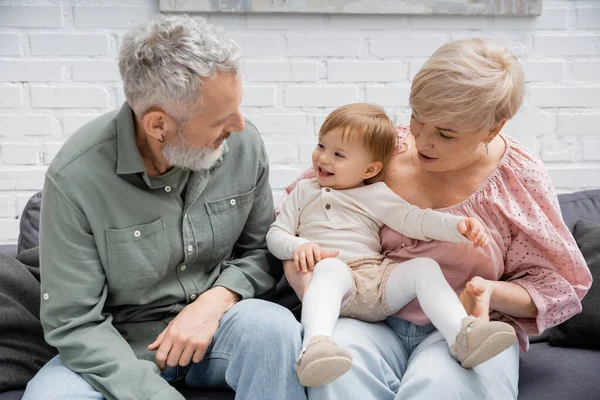 Overjoyed kid smiling near granny and grandpa sitting on sofa in living room — Stock Photo