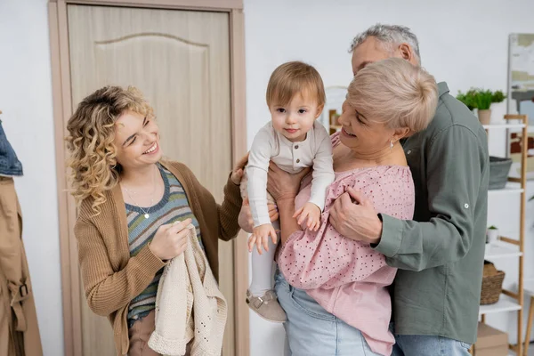 Щаслива жінка середнього віку тримає маленьку онучку біля сім'ї та вхідних дверей вдома — стокове фото