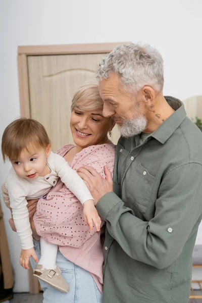 Jubelnde Frau umarmt kleine Enkelin neben bärtigem Ehemann im Hausflur — Stockfoto