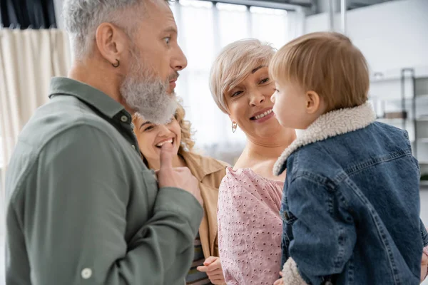 Смешной бородатый мужчина гримасит рядом с маленькой внучкой и веселой семьей дома — стоковое фото
