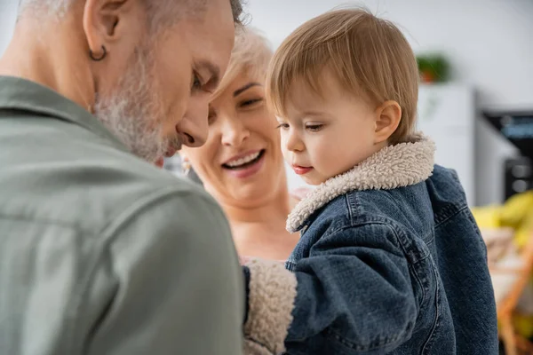 Happy middle aged woman smiling near toddler granddaughter and husband at home — Stock Photo
