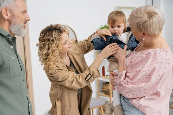 Smiling blonde woman undressing daughter while visiting grandparents at home — Stock Photo