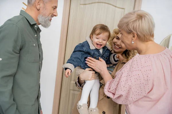 Überglückliches Kind in Jeansjacke lächelt bei Mutter und Großeltern vor Haustür — Stockfoto