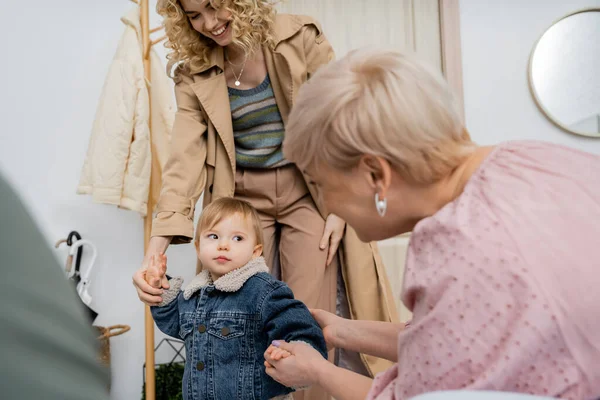 Mujer de mediana edad cogida de la mano de la nieta en chaqueta de mezclilla mientras se reúne en casa - foto de stock