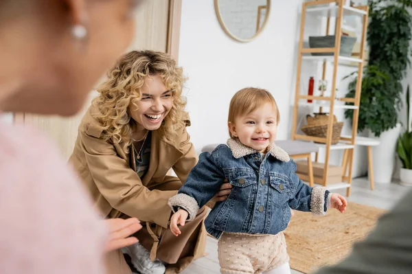 Весела дитина в джинсовій куртці посміхається біля щасливої матері і бабусі на розмитому передньому плані — стокове фото
