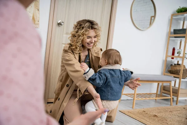 Mulher alegre em casaco de trincheira reunião criança filha perto da porta de entrada em casa — Fotografia de Stock