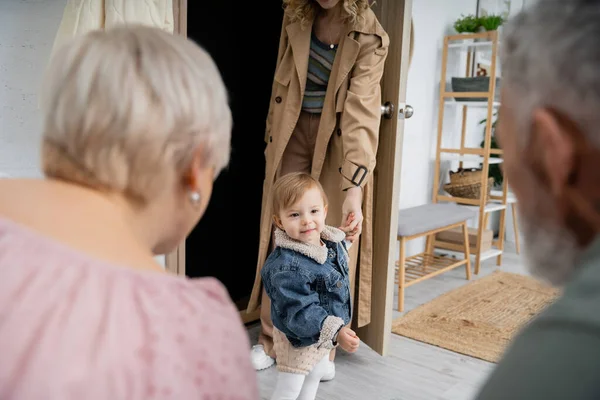 Blurred middle aged couple meeting daughter with little child at home — Stock Photo