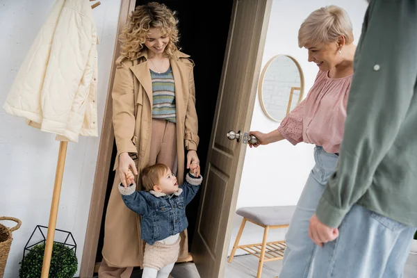 Щаслива жінка середнього віку відкриває двері доньці з дівчинкою-малюком вдома — стокове фото