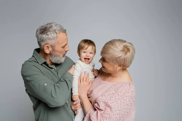 Excited baby girl laughing near happy grandparents isolated on grey — Stock Photo