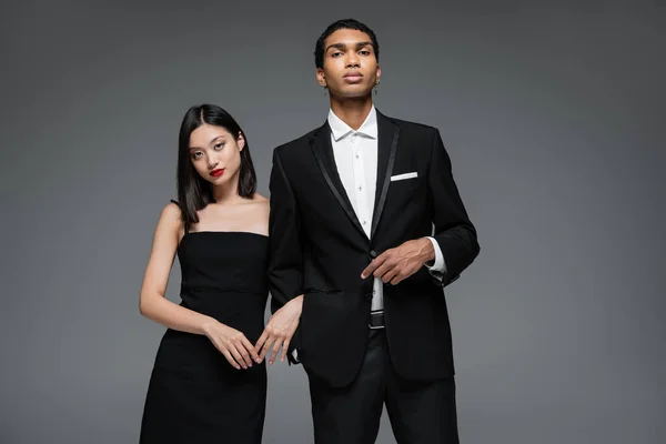 Giovane coppia interrazziale in elegante abbigliamento formale guardando la fotocamera isolata sul grigio — Foto stock