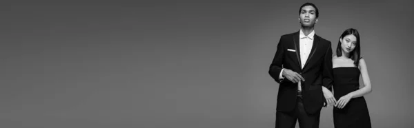 Jeunes modèles interracial en noir élégant vêtements regardant caméra isolé sur gris, bannière — Photo de stock