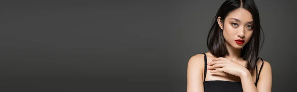 Ritratto di donna asiatica alla moda con labbra rosse guardando la fotocamera isolata su grigio, banner — Foto stock