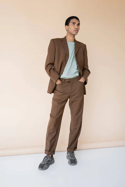 Comprimento total do homem afro-americano em ternos da moda de pé com as mãos nos bolsos e olhando para o fundo bege — Fotografia de Stock