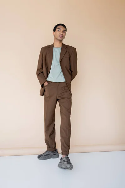 Full length of african american man in brown suit standing with hand in pocket on beige background — Stock Photo