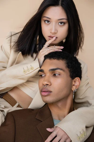 Moda asiático mujer tocando labios cerca joven africano americano hombre aislado en beige - foto de stock