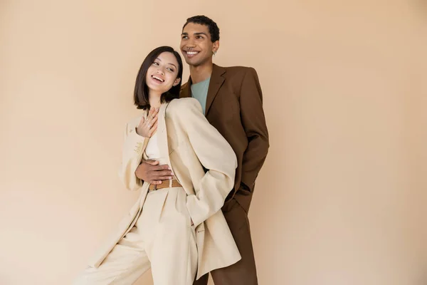 Positif afro-américain homme embrassant excité asiatique femme en ivoire costume isolé sur beige — Photo de stock