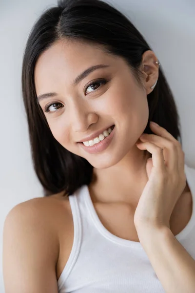 Портрет беззаботной азиатской женщины с идеальной кожей и натуральным макияжем, смотрящей на камеру, изолированную на сером — стоковое фото
