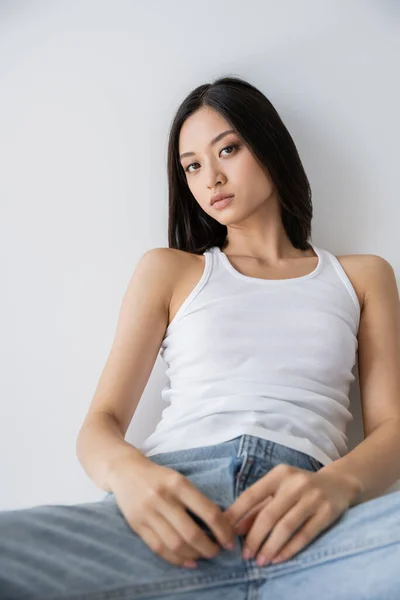 Hübsche asiatische Frau posiert in weißem Tank-Top und blauen Jeans auf grauem Hintergrund — Stockfoto
