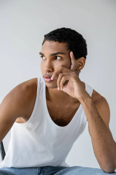 Pensoso afroamericano in canotta bianca che tiene la mano vicino al viso e distoglie lo sguardo isolato sul grigio — Foto stock