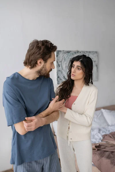 Morena mujer calmando molesto novio en pijama en el dormitorio - foto de stock