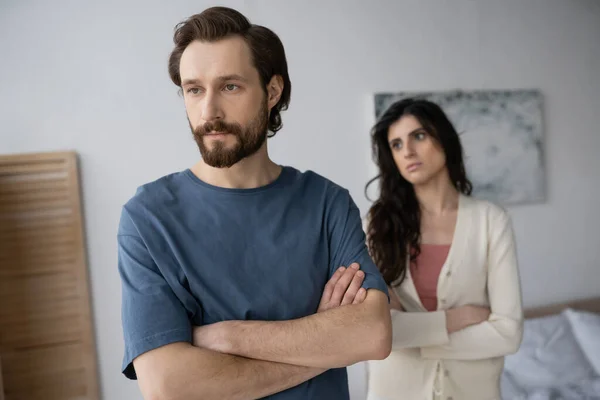 Sad man crossing arms near blurred girlfriend in bedroom at home — Stock Photo