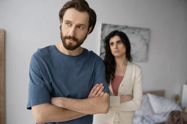 Offended man crossing arms near blurred girlfriend in bedroom — Stock Photo