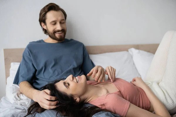 Overjoyed woman in pajama lying near blurred boyfriend on bed at home — Stock Photo