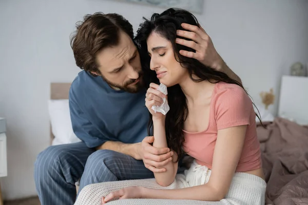 Caring man in pajama hugging crying and upset girlfriend on bed at home — Stock Photo