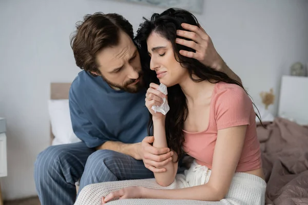 Homme attentionné en pyjama étreignant pleurer et bouleversé petite amie sur le lit à la maison — Photo de stock