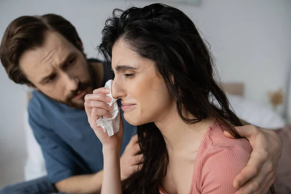 Mujer disgustada llorando cerca de cuidar novio borroso en casa - foto de stock