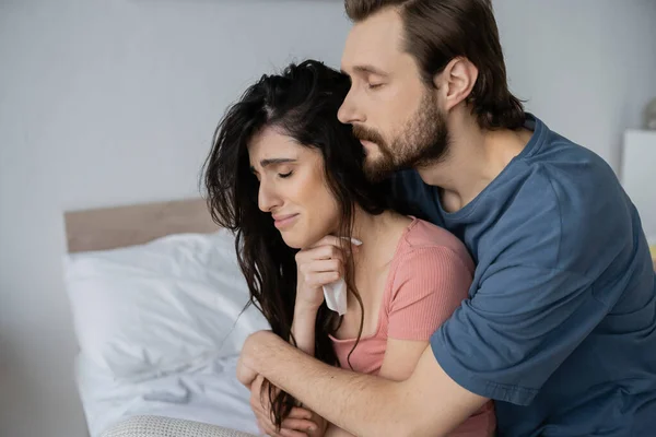 Barbudo hombre abrazando novia insatisfecha con servilleta en el dormitorio - foto de stock