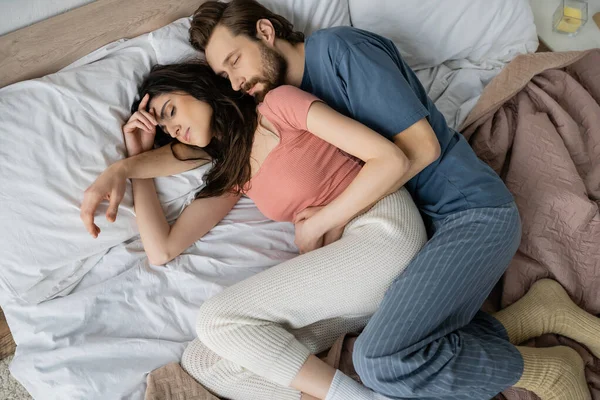 Top view of man in pajama hugging girlfriend while sleeping on bed — Stock Photo