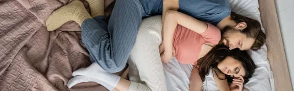 Вид зверху незадоволений чоловік обіймає подругу в піжамі на ліжку, банер — стокове фото