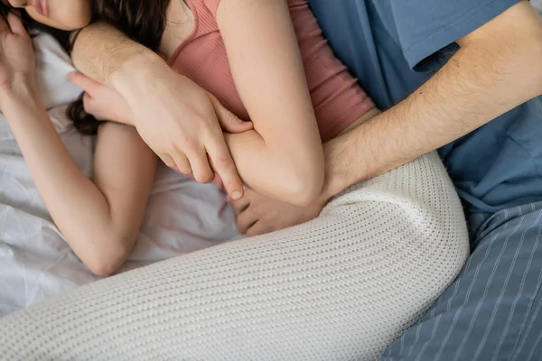 Cropped view of man hugging girlfriend in pajama on bed at home — Stock Photo
