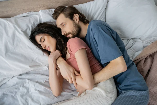 Top view of man in pajama hugging sleeping girlfriend on bed at home — Stock Photo