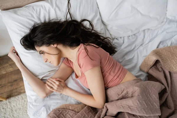 Draufsicht der traurigen brünetten Frau, die morgens auf dem Bett liegt — Stockfoto