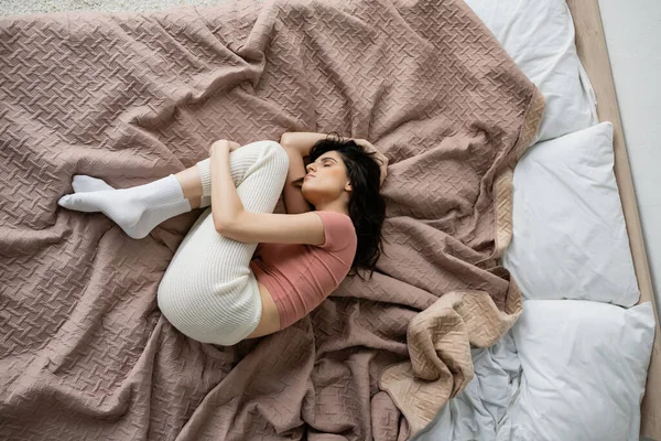 Вид сверху одинокой женщины в пижаме, лежащей на кровати дома — стоковое фото