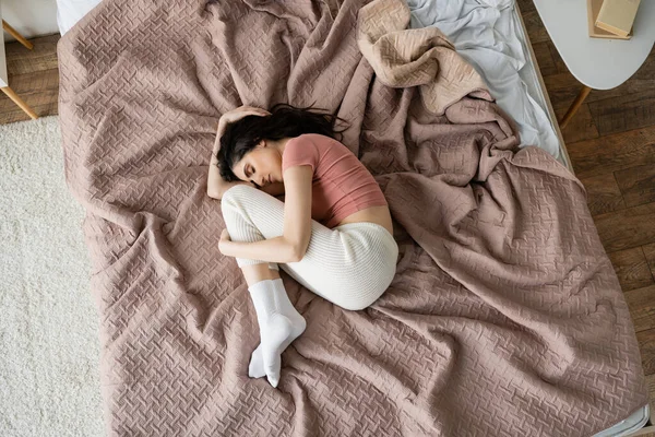 Вид сверху на расстроенную женщину в пижаме, лежащую на кровати дома — стоковое фото