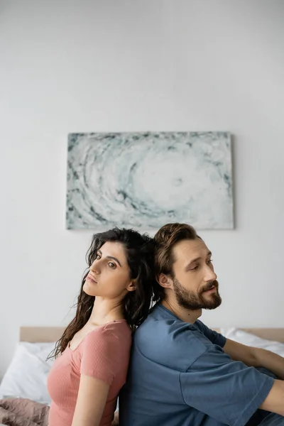Couple bouleversé en pyjama assis dos à dos sur le lit à la maison — Photo de stock