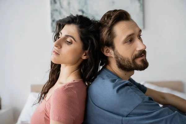 Triste pareja sentada espalda con espalda en el dormitorio borroso en casa - foto de stock
