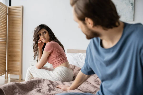 Brunette woman in pajama looking at blurred boyfriend on bed at home — Stock Photo