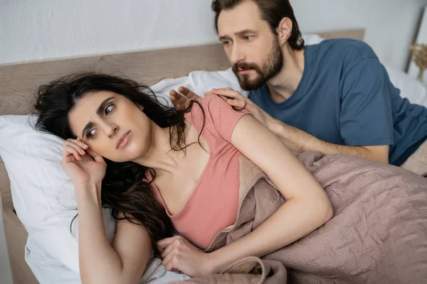 Sad woman lying near blurred boyfriend on bed at home — Stock Photo