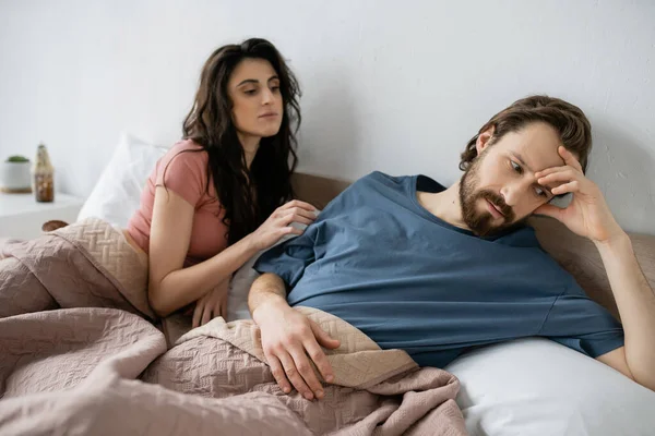 Напружений асексуальний чоловік сидить біля розмитої дівчини на ліжку вдома — стокове фото