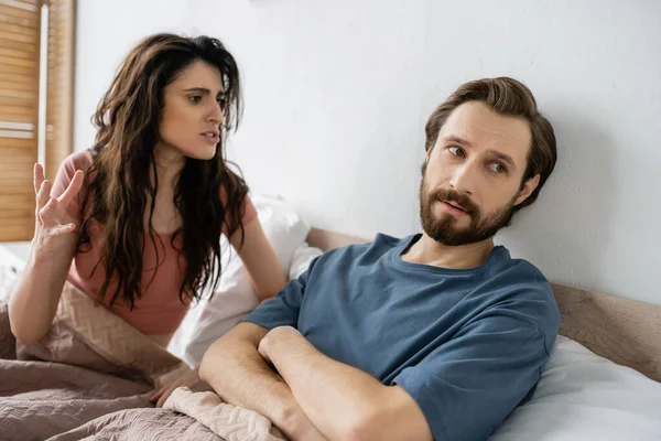 Злая женщина разговаривает с бородатым парнем, скрещивая руки на кровати дома — стоковое фото
