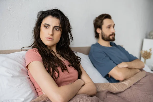 Nervous woman crossing arms while sitting near blurred boyfriend on bed — Stock Photo