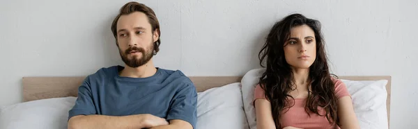 Недовольная пара с трудностями в отношениях, сидя на кровати дома, баннер — стоковое фото